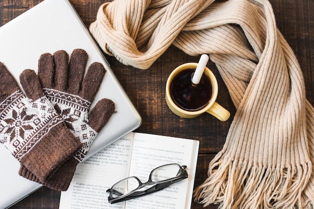 Heißer Tee und warme Accessoires in der Nähe von Laptop und Buch