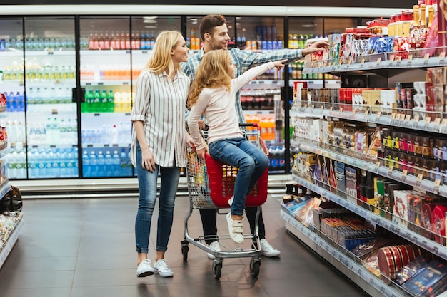 Heiteres kleines Mädchen, das auf einem Einkaufswagen sitzt