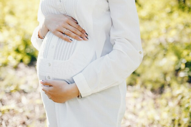 helle und glückliche schwangere Frau, die in den sonnigen Park geht