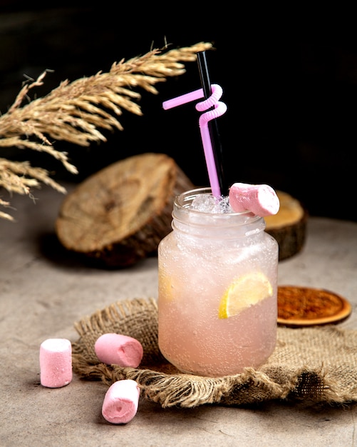 Hellrosa kohlensäurehaltiges Getränk mit Zitronenscheibe, garniert mit Marshmellow