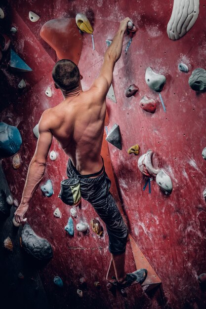 Hemdloser athletischer Mann, der an einer roten Indoor-Kletterwand klettert.