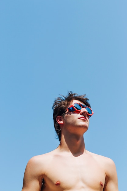 Hemdloser junger Mann mit Schwimmbrille gegen blauen Himmel