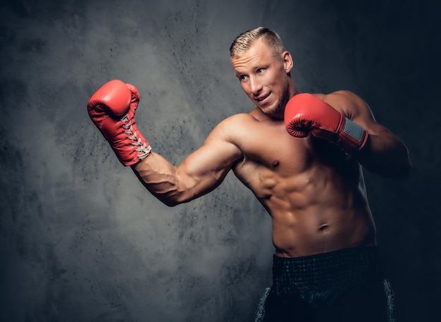 Hemdloser Kickboxer, der seine Schläge und Tritte auf grauem Hintergrund in einem Studio zeigt.