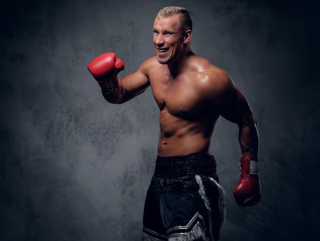 Hemdloser Kickboxer, der seine Schläge und Tritte auf grauem Hintergrund in einem Studio zeigt.