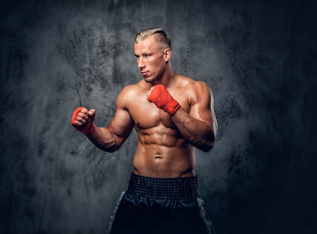 Hemdloser Kickboxer, der seine Schläge und Tritte auf grauem Hintergrund in einem Studio zeigt.