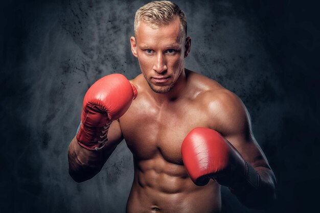 Hemdloser Kickboxer, der seine Schläge und Tritte auf grauem Hintergrund in einem Studio zeigt.