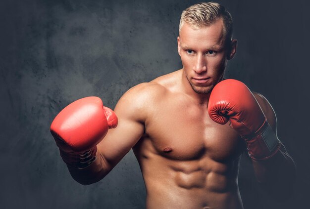 Hemdloser Kickboxer, der seine Schläge und Tritte auf grauem Hintergrund in einem Studio zeigt.