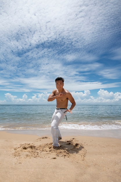 Hemdloser Mann, der Capoeira am Strand praktiziert