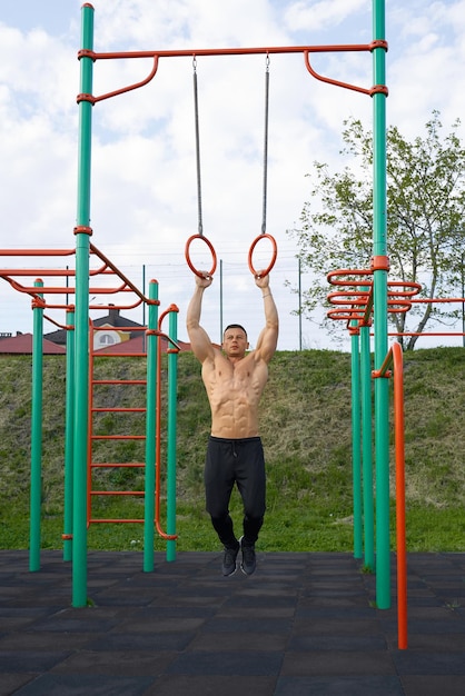 Hemdloser Mann, der im Freien Klimmzüge an Turnringen macht