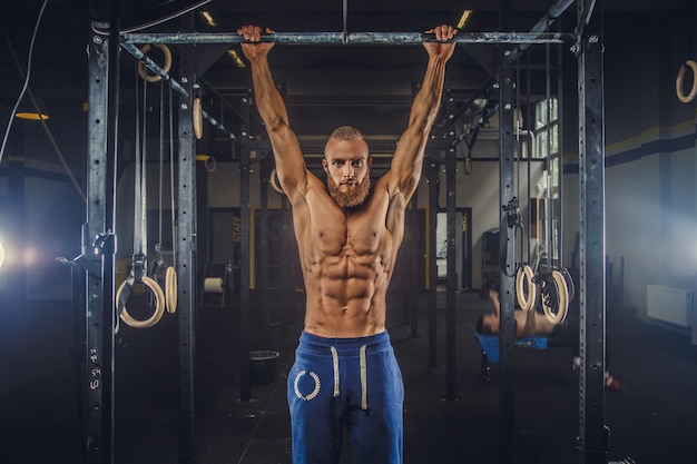 Hemdloser, muskulöser, bärtiger Mann, der Übungen an der horizontalen Stange in einem Fitnessstudio macht.