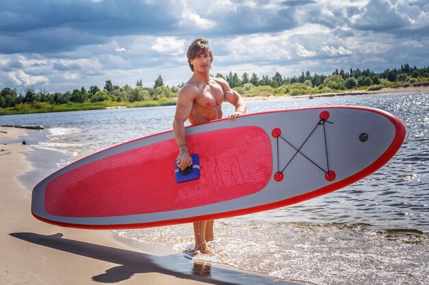 Hemdloser Surfer mit muskulösem Körper und seinem Surfbrett am Strand.