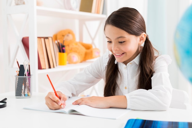 Herausgenommenes nettes Schulmädchen in der Uniform zu Hause studierend