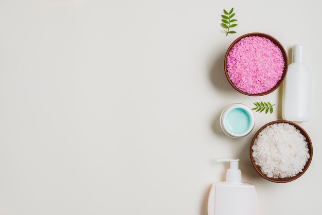 Herbales rosa und weißes Salz rollt mit kosmetischen Produkten auf weißem Hintergrund