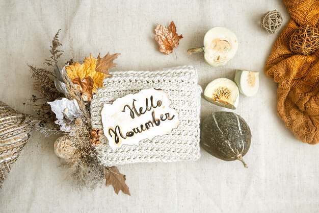 Herbstkomposition mit getrockneten Blumen, Kürbis und Strickelement in der Mitte auf weißem Hintergrund.