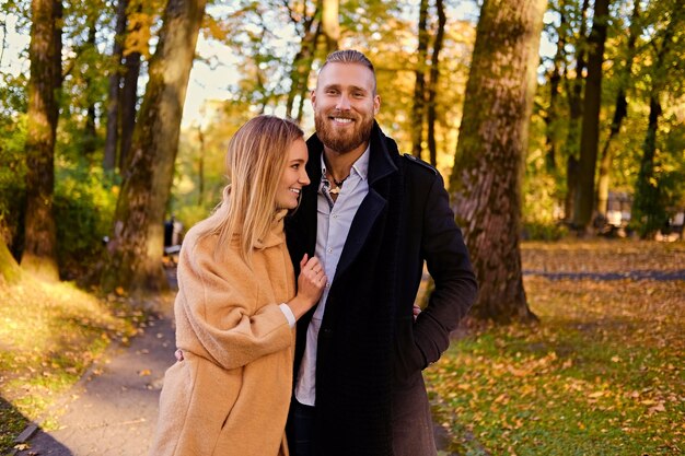 Herbstliche Liebesgeschichte. Rothaariger bärtiger Mann umarmt die süße blonde Frau beim Date in einem Herbstpark.