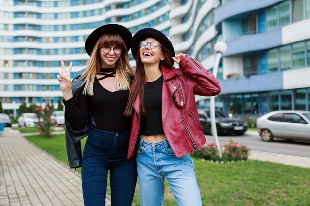 Herbstmode-Look. Paar attraktive anmutige Mädchen in niedlichen runden Gläsern und schwarzen Hüten, die aufwerfen