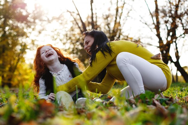 Herbststimmung, Familienportrait. Bezaubernde Mutter und ihre rote Haartochter haben Spaß beim Sitzen auf dem Gefallenen