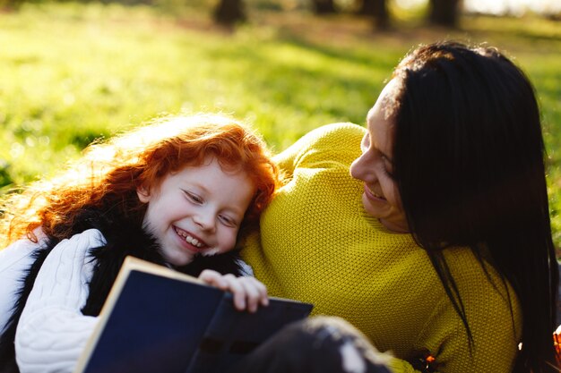 Herbststimmung, Familienportrait. Bezaubernde Mutter und ihre rote Haartochter haben Spaß beim Sitzen auf dem Gefallenen
