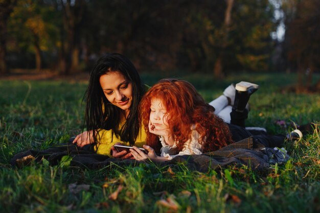 Herbststimmung, Familienportrait. Bezaubernde Mutter und ihre rote Haartochter haben Spaß beim Sitzen auf dem Gefallenen