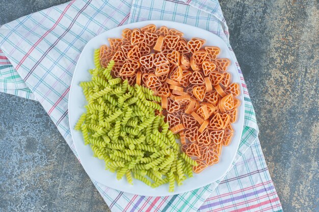 Herdförmige Nudeln mit Fusilli-Nudeln im Teller, auf dem Handtuch, auf der Marmoroberfläche.