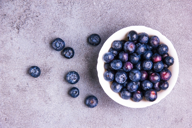 Kostenloses Foto herrliche blaubeeren in einer weißen runden schüssel auf einem violetten gipshintergrund. flach liegen.