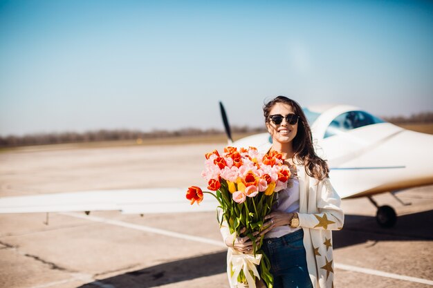 Herrlicher Brunette steht mit großem Blumenstrauß von Tulpen vor einem Flugzeug