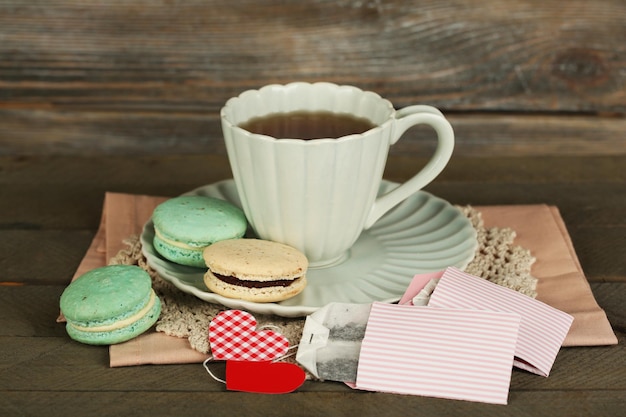 Herzförmige teebeutel-tags, makronen und eine tasse tee auf holzhintergrund