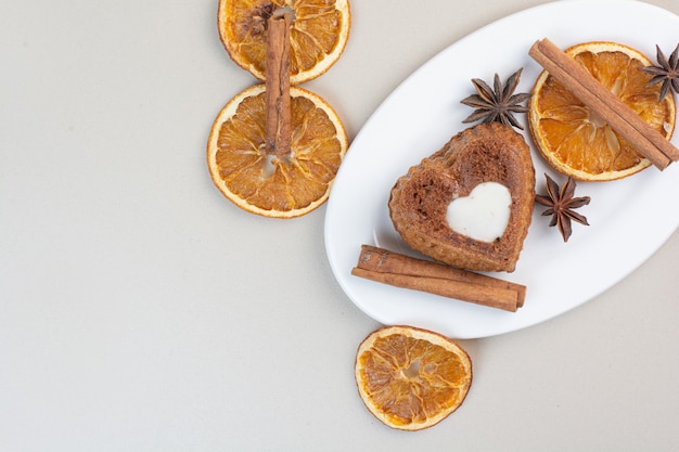 Kostenloses Foto herzförmiger cremiger kuchen mit orangenscheiben, nelken und zimt auf weißem teller