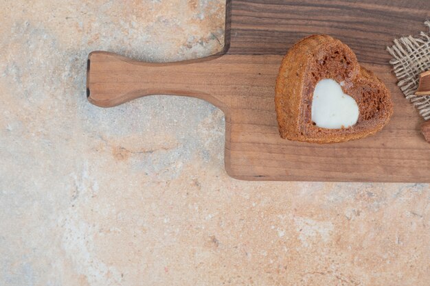 Kostenloses Foto herzförmiger kuchen mit sahne auf holzbrett.