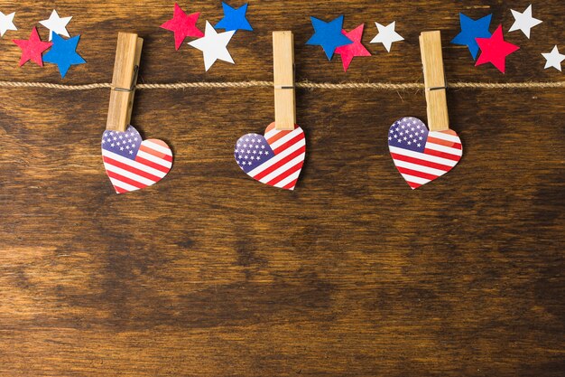 Herzformen amerikanischer Flagge USA hängen an den Wäscheklammern, die mit Sternen auf hölzernem Schreibtisch verziert werden