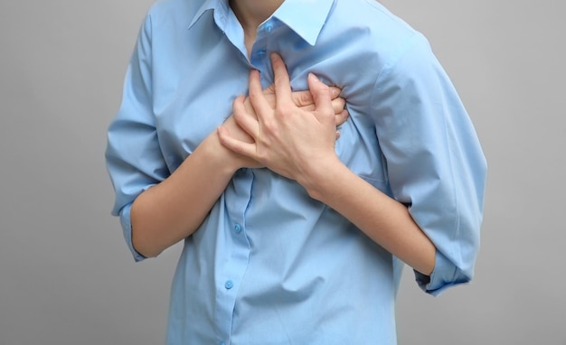 Herzinfarkt-konzept. junge frau mit brustschmerzen auf grauem hintergrund