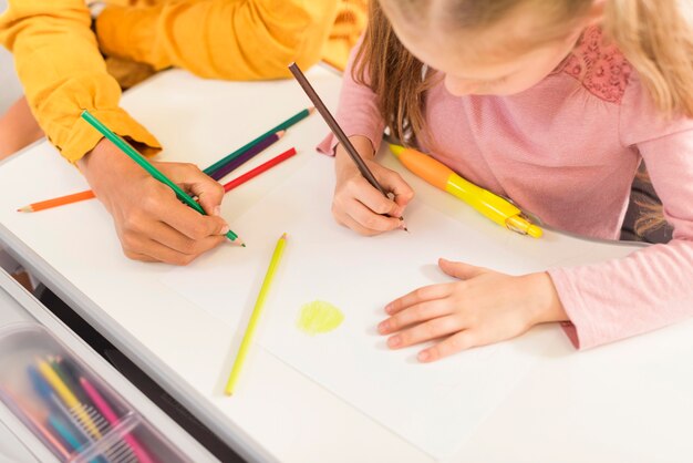 High Angle Lehrer hilft einem Schüler in der Klasse