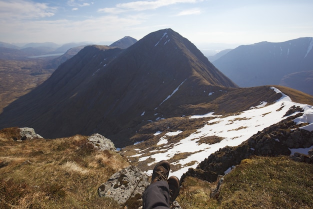 High Angle Shot der Beine eines Menschen, der auf dem Boden oben auf den Bergen sitzt