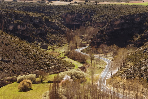 High Angle Shot einer kurvigen Straße, umgeben von felsigen Klippen und wunderschönem Grün