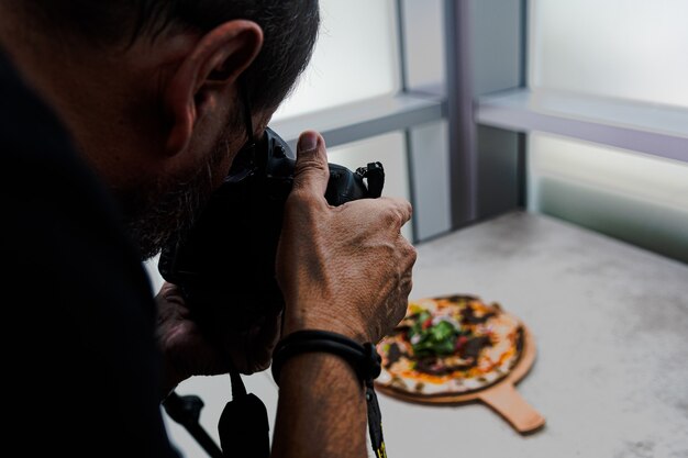 High Angle Shot einer Person, die ein Foto von einer Pizza auf dem Tisch macht