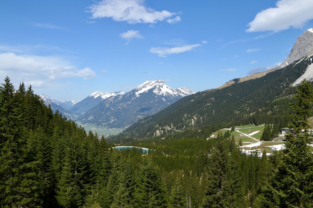 High Angle Shot einer schönen Bergkette mit grünen Tannen und Schnee unter bewölktem Himmel bedeckt