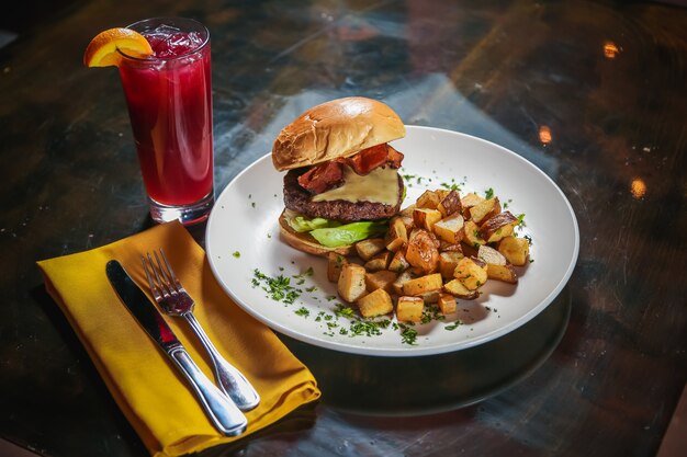 High Angle Shot eines Cheeseburger mit Kartoffelwürfeln an der Seite mit einem roten Getränk daneben