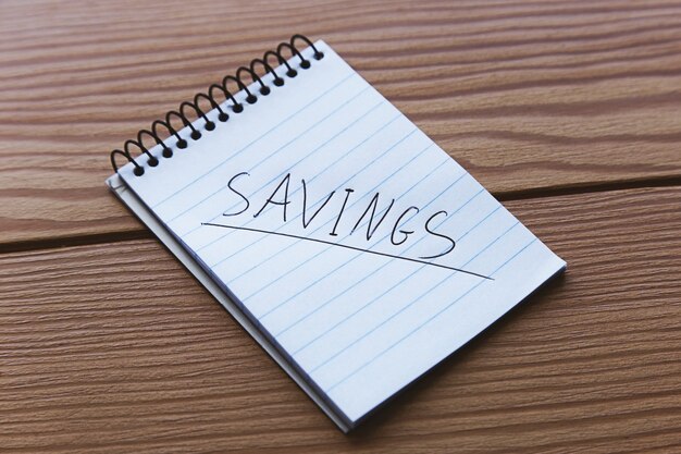 High Angle Shot eines kleinen Notizbuchs mit dem Wort Savings auf einer Holzoberfläche