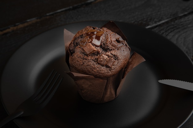 High Angle Shot eines Schokoladenmuffins auf einem schwarzen Teller auf einem dunklen Holztisch