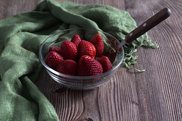 High Angle Shot von frischen Erdbeeren und einem grünen Textil in einer Glasschale auf einer Holzoberfläche