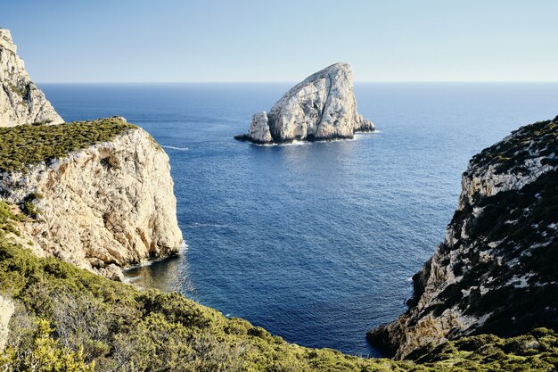 High Angle Shot von grasbewachsenen Klippen in der Nähe des Meeres mit einem Felsen in der Ferne
