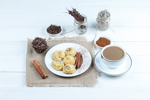 High Angle View Cookies, Zimt, Seile auf Stück Sack mit Schüssel Instantkaffee, Tasse Kaffee auf weißem Holzbrett Hintergrund. horizontal