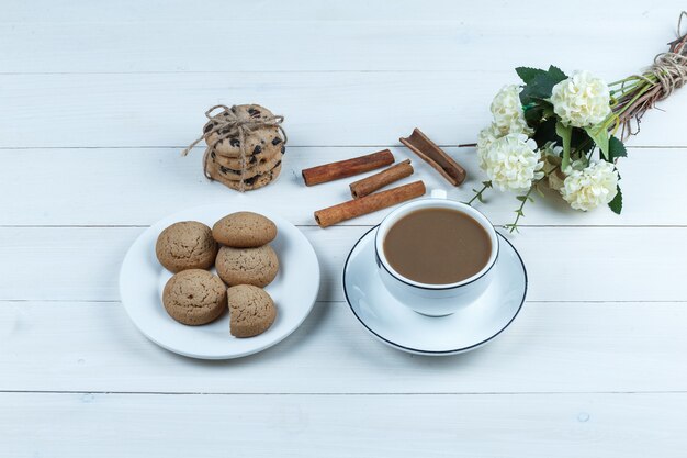 High Angle View Tasse Kaffee mit Blumen, Zimt, verschiedene Arten von Keksen auf weißem Holzbrett Hintergrund. horizontal