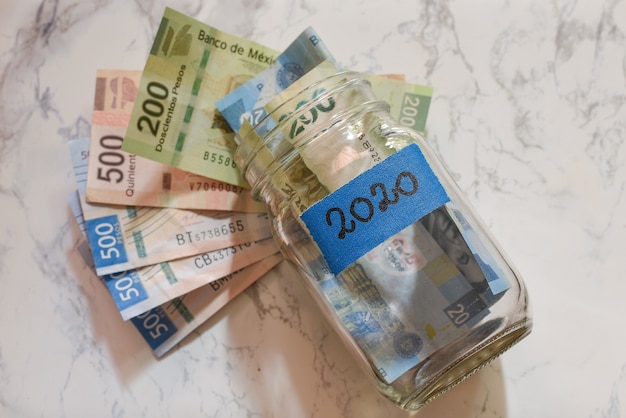 High Angle View von Pesos in einem Glas mit einem blauen [2020] Etikett auf dem Tisch unter den Lichtern