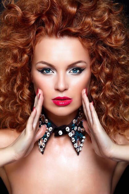 High Fashion Look.glamour Nahaufnahme Porträt der schönen sexy rothaarigen kaukasischen jungen Frau Modell mit roten Lippen, helles Make-up, mit perfekter sauberer Haut mit Schmuck auf schwarz isoliert