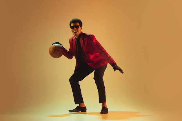 Kostenloses Foto highfashion gestylter mann in roter jacke, der basketball spielt, isoliert auf braunem hintergrund