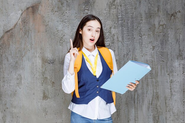 Highschool-Mädchen mit gelbem Rucksack und Ordnerzeigen. Foto in hoher Qualität