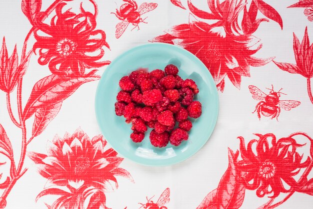 Himbeeren auf blauer Platte über der Blumentischdecke