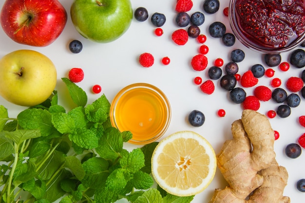 Kostenloses Foto himbeeren mit honig, äpfeln, blaubeeren, roten johannisbeeren, zitrone, ingwer, minze lässt draufsicht auf einer weißen oberfläche