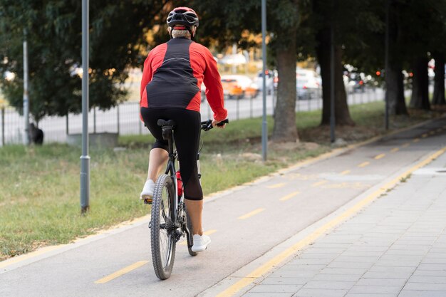Hintere ansicht der älteren frau, die fahrrad im freien mit kopienraum reitet